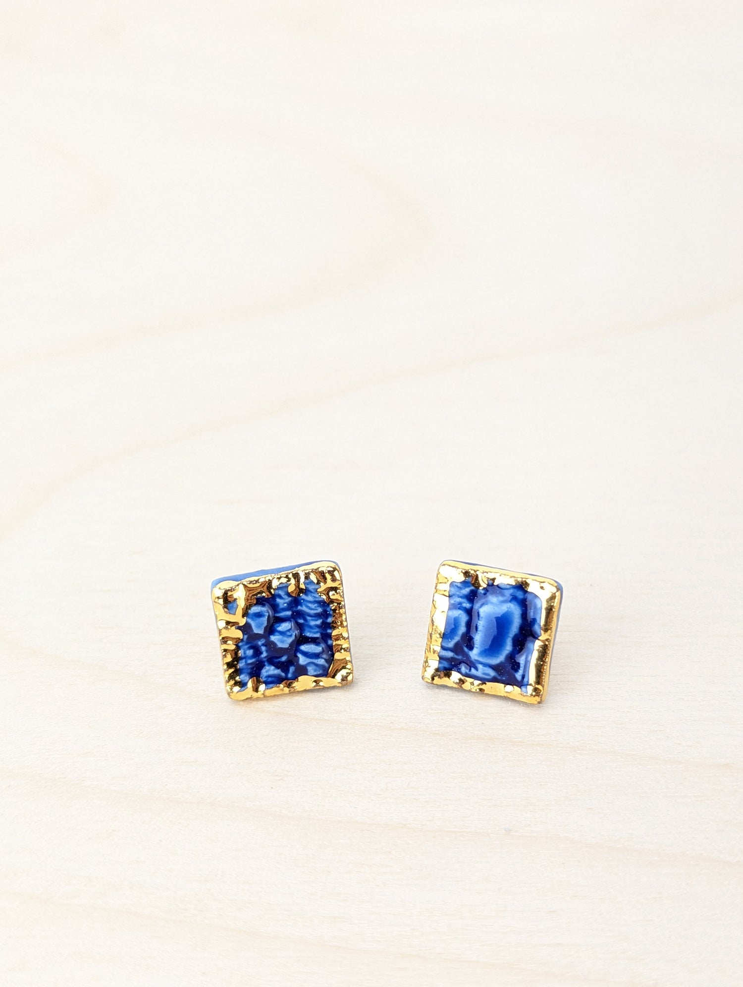 small square stud earrings in cobalt blue with a lace texture imprinted in the surface and a gold edge