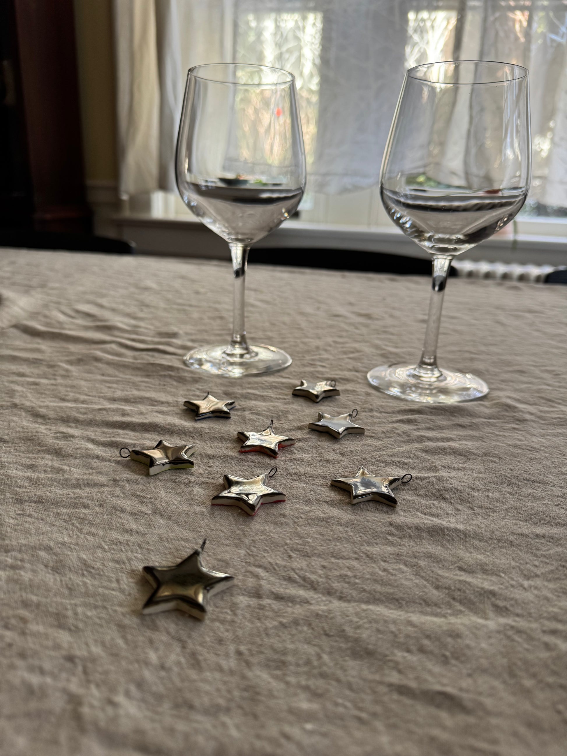 Two empty wine glasses on a textured surface with silver star-shaped drink charms in front.