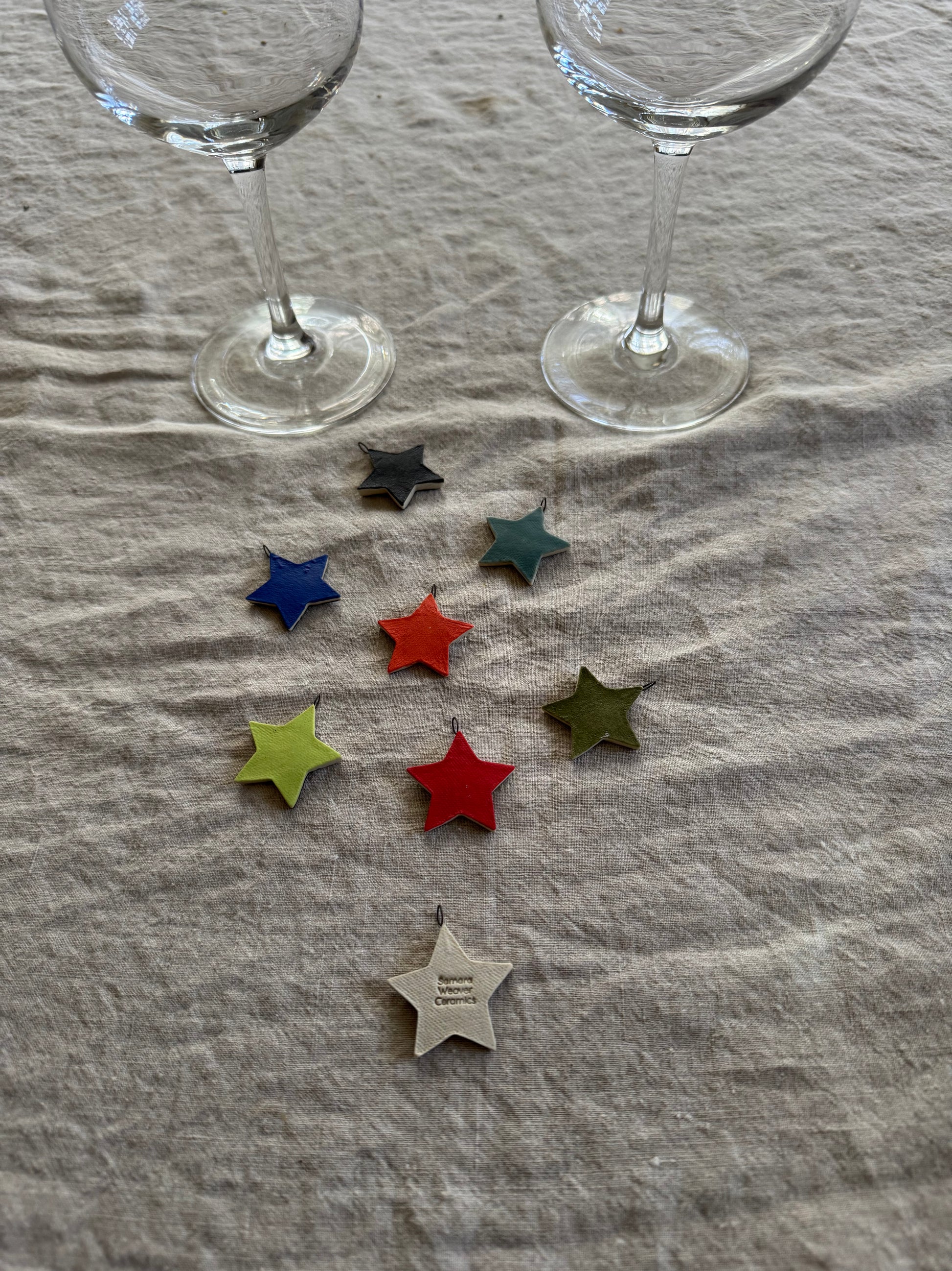 Colorful star-shaped drink charms on a textured surface with two clear wine glasses.