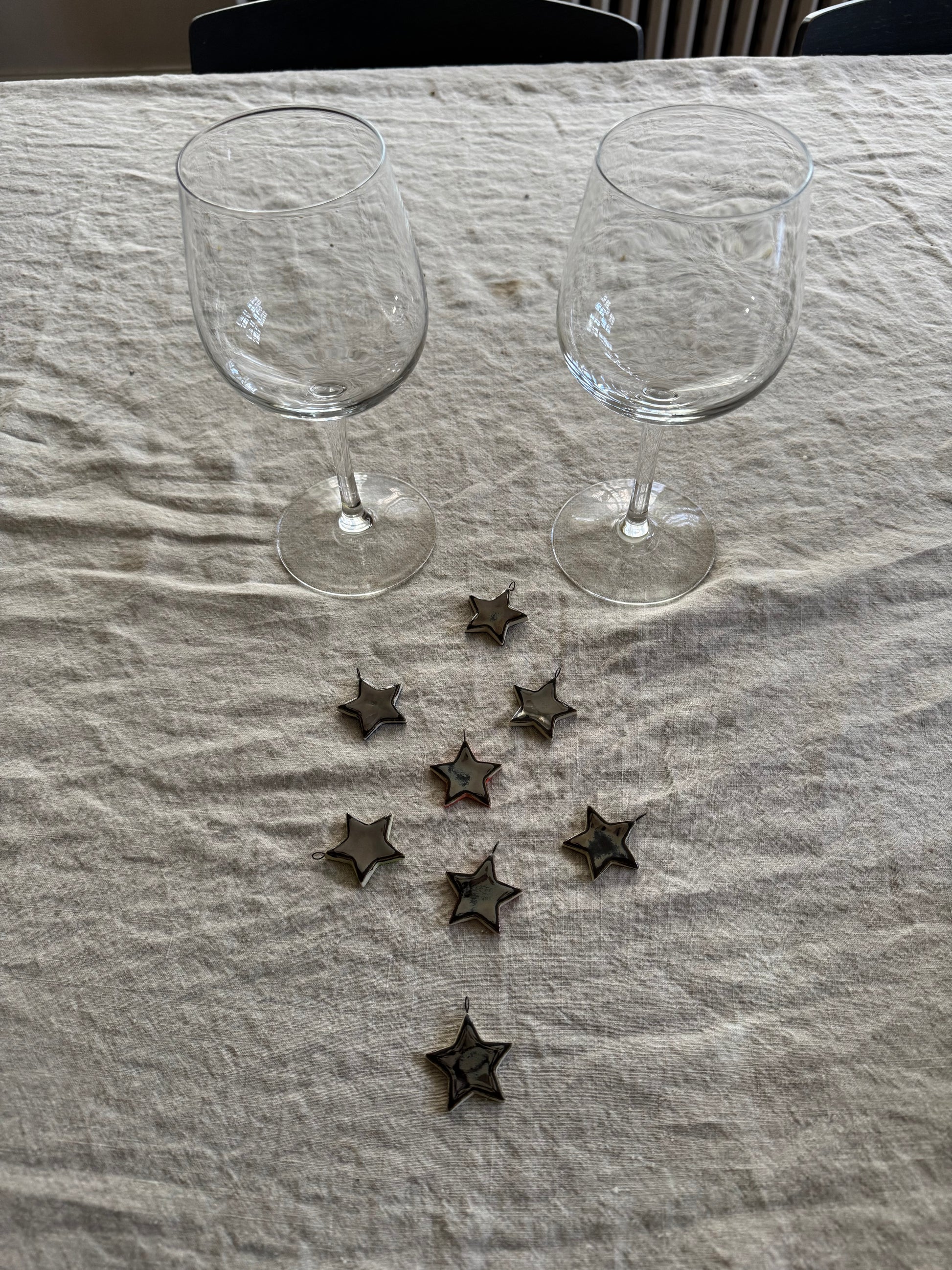 Two clear wine glasses on a textured surface with decorative silver star charms around them.