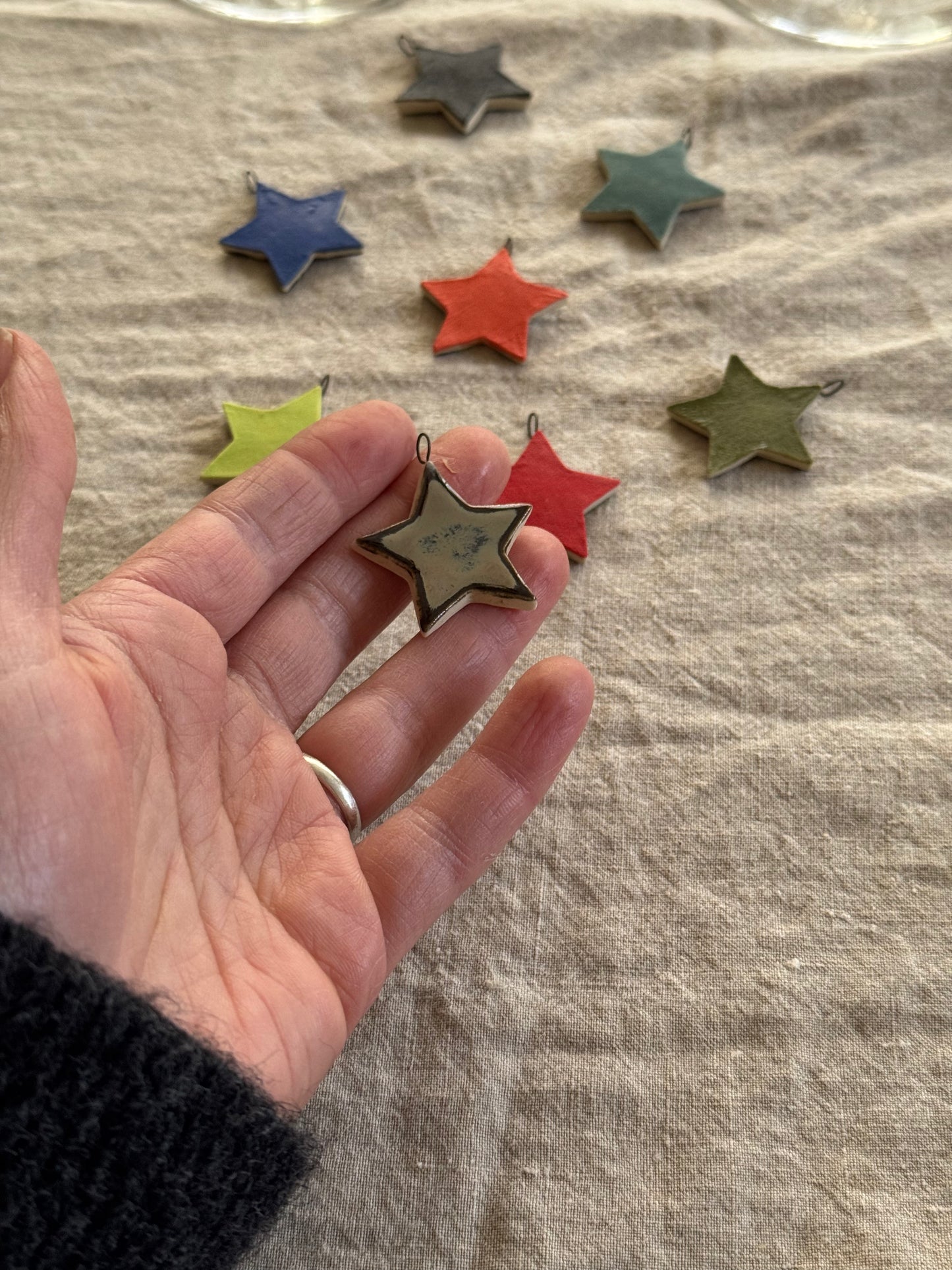 Hand holding a star-shaped wine charm with other colorful star drink charms on a textured fabric background