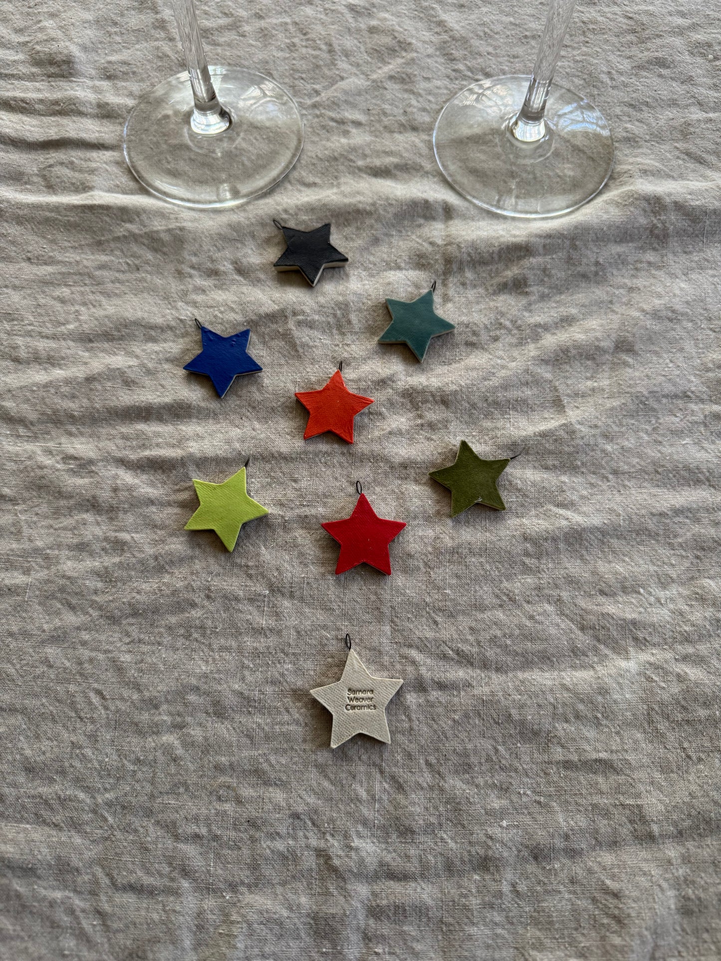 Colorful star-shaped wine charms on a textured fabric surface with two wine glasses in the background.