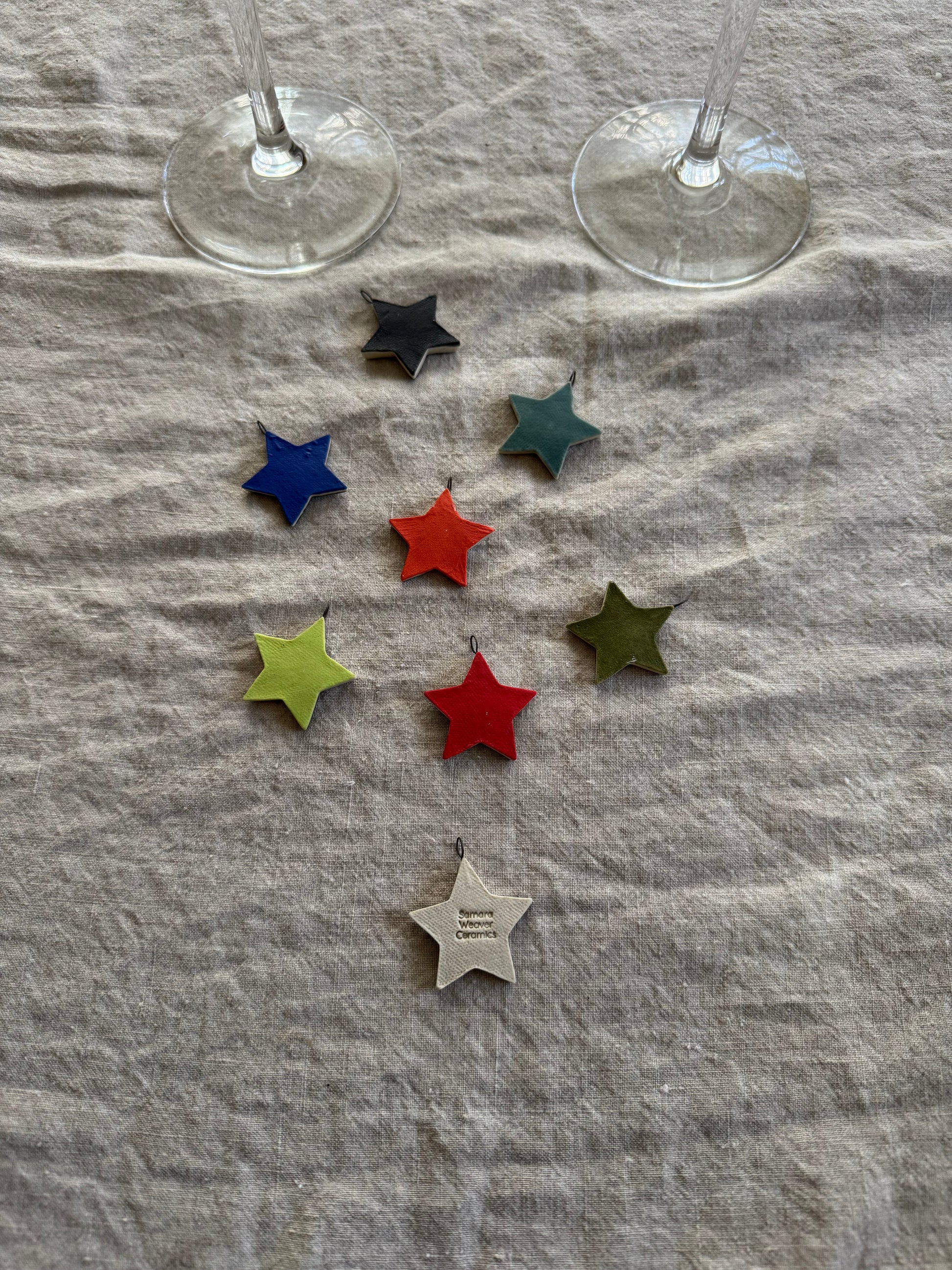 Colorful star-shaped wine charms on a textured fabric surface with two wine glasses in the background.
