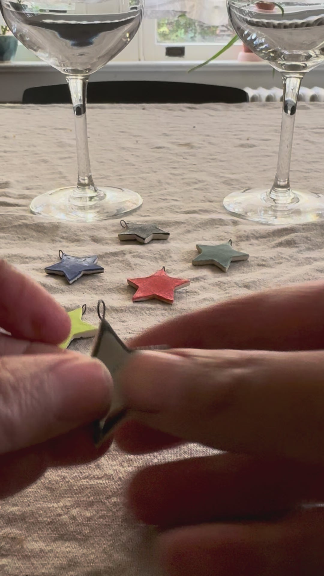 A video of hands connecting a round silver loop to the star shaped drink charms to show how they can be attached to a wine glass stem. more star charms and two wine glasses in the background. 
